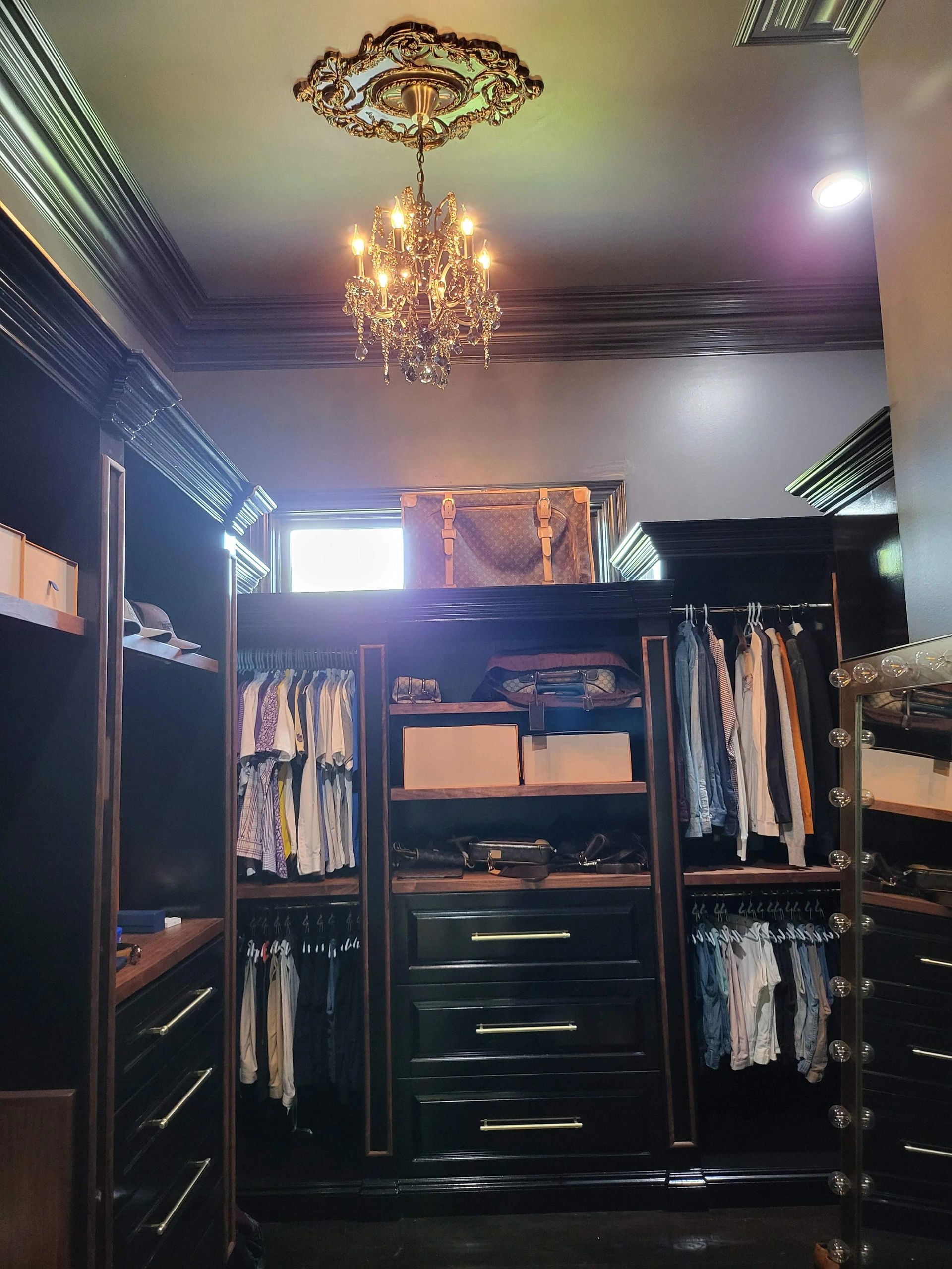 Custom dark wood closet beneath a decorative chandelier